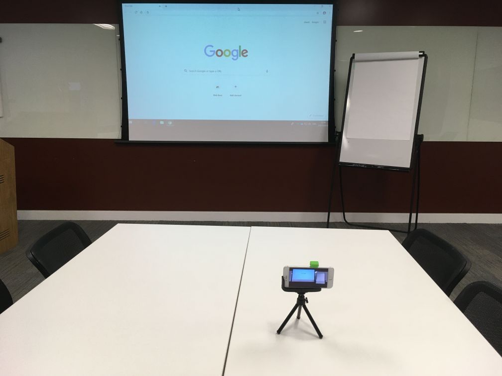 A smartphone on a small tripod on top of a table about waist height